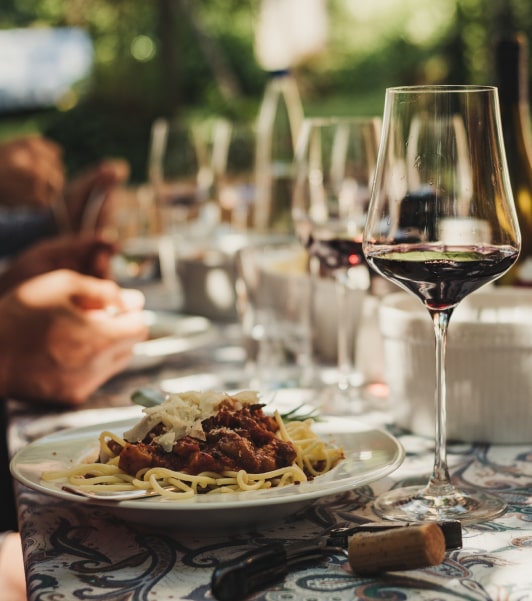 Gedeckte Tafel im Garten mit Rotweingläsern und Tellern mit Spaghetti Bolognese