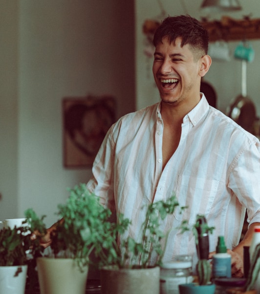 Lachender Mann in einer Küche , davor einige Kräuterpflanzen