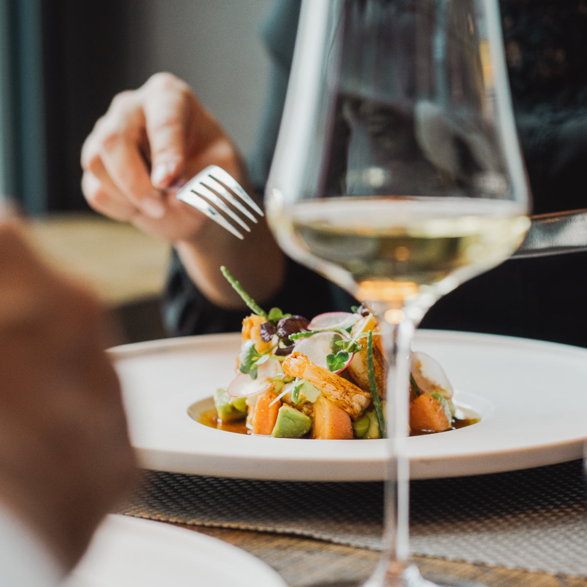 Ein Gericht eines Fine-Dining Restaurants, davor ein Glas Weißwein