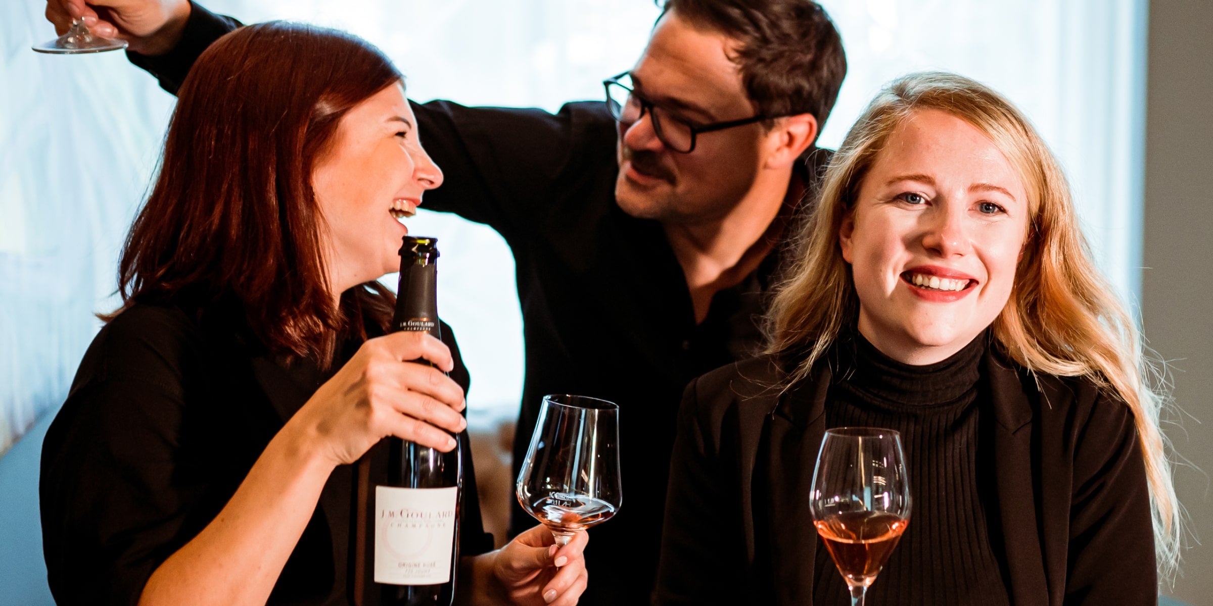 Zwei Frauen und ein Mann lachend bei einem Glas Wein